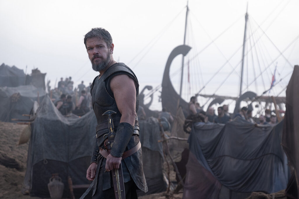 Let me say the quiet part loudly: Christopher Nolan did not make a swords-and-sandals adventure. He made a war film wearing a myth as a mask, and it may be the most punishing, beautiful thing he has ever put on a screen. The Odyssey is his thirteenth feature, the first narrative film in history shot entirely on IMAX film, and already the biggest global launch of his career — an instant awards frontrunner that had the industry roaring from its first CinemaCon footage onward, in a year that suddenly has very little competition. Coming off Oppenheimer, Nolan has essentially made a companion piece in bronze: another story about a brilliant man whose single clever idea unleashes a horror the world cannot put back in the box. If Oppenheimer gave us the father of the atomic bomb, The Odyssey gives us his Bronze Age ancestor.