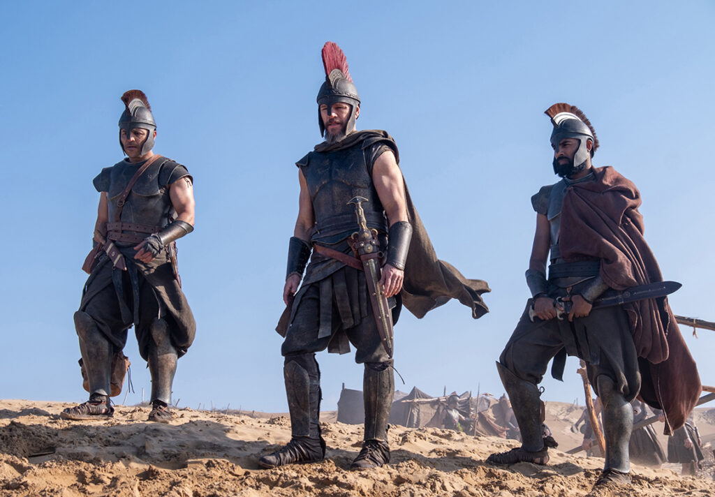 Let me say the quiet part loudly: Christopher Nolan did not make a swords-and-sandals adventure. He made a war film wearing a myth as a mask, and it may be the most punishing, beautiful thing he has ever put on a screen. The Odyssey is his thirteenth feature, the first narrative film in history shot entirely on IMAX film, and already the biggest global launch of his career — an instant awards frontrunner that had the industry roaring from its first CinemaCon footage onward, in a year that suddenly has very little competition. Coming off Oppenheimer, Nolan has essentially made a companion piece in bronze: another story about a brilliant man whose single clever idea unleashes a horror the world cannot put back in the box. If Oppenheimer gave us the father of the atomic bomb, The Odyssey gives us his Bronze Age ancestor.