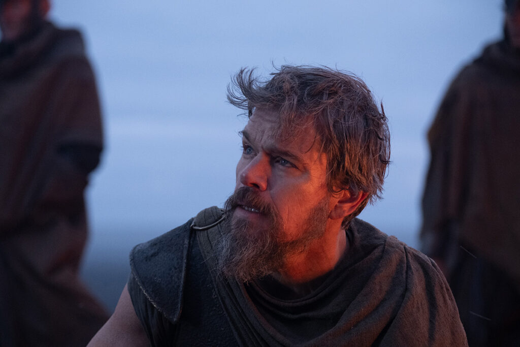 Let me say the quiet part loudly: Christopher Nolan did not make a swords-and-sandals adventure. He made a war film wearing a myth as a mask, and it may be the most punishing, beautiful thing he has ever put on a screen. The Odyssey is his thirteenth feature, the first narrative film in history shot entirely on IMAX film, and already the biggest global launch of his career — an instant awards frontrunner that had the industry roaring from its first CinemaCon footage onward, in a year that suddenly has very little competition. Coming off Oppenheimer, Nolan has essentially made a companion piece in bronze: another story about a brilliant man whose single clever idea unleashes a horror the world cannot put back in the box. If Oppenheimer gave us the father of the atomic bomb, The Odyssey gives us his Bronze Age ancestor.