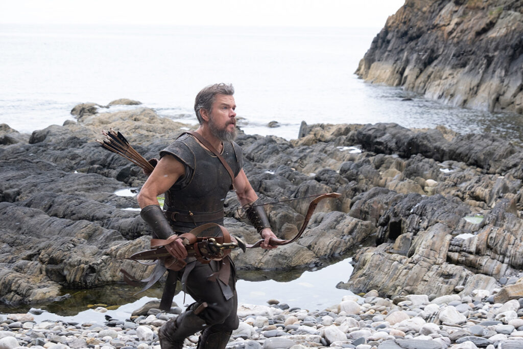 Let me say the quiet part loudly: Christopher Nolan did not make a swords-and-sandals adventure. He made a war film wearing a myth as a mask, and it may be the most punishing, beautiful thing he has ever put on a screen. The Odyssey is his thirteenth feature, the first narrative film in history shot entirely on IMAX film, and already the biggest global launch of his career — an instant awards frontrunner that had the industry roaring from its first CinemaCon footage onward, in a year that suddenly has very little competition. Coming off Oppenheimer, Nolan has essentially made a companion piece in bronze: another story about a brilliant man whose single clever idea unleashes a horror the world cannot put back in the box. If Oppenheimer gave us the father of the atomic bomb, The Odyssey gives us his Bronze Age ancestor.