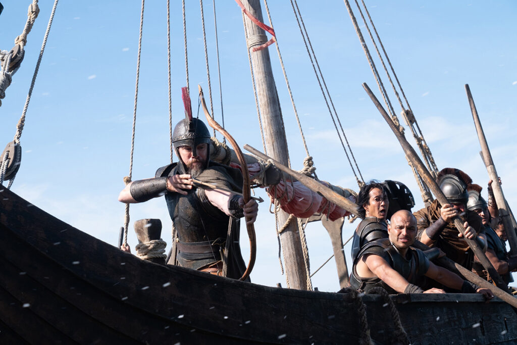 Let me say the quiet part loudly: Christopher Nolan did not make a swords-and-sandals adventure. He made a war film wearing a myth as a mask, and it may be the most punishing, beautiful thing he has ever put on a screen. The Odyssey is his thirteenth feature, the first narrative film in history shot entirely on IMAX film, and already the biggest global launch of his career — an instant awards frontrunner that had the industry roaring from its first CinemaCon footage onward, in a year that suddenly has very little competition. Coming off Oppenheimer, Nolan has essentially made a companion piece in bronze: another story about a brilliant man whose single clever idea unleashes a horror the world cannot put back in the box. If Oppenheimer gave us the father of the atomic bomb, The Odyssey gives us his Bronze Age ancestor.