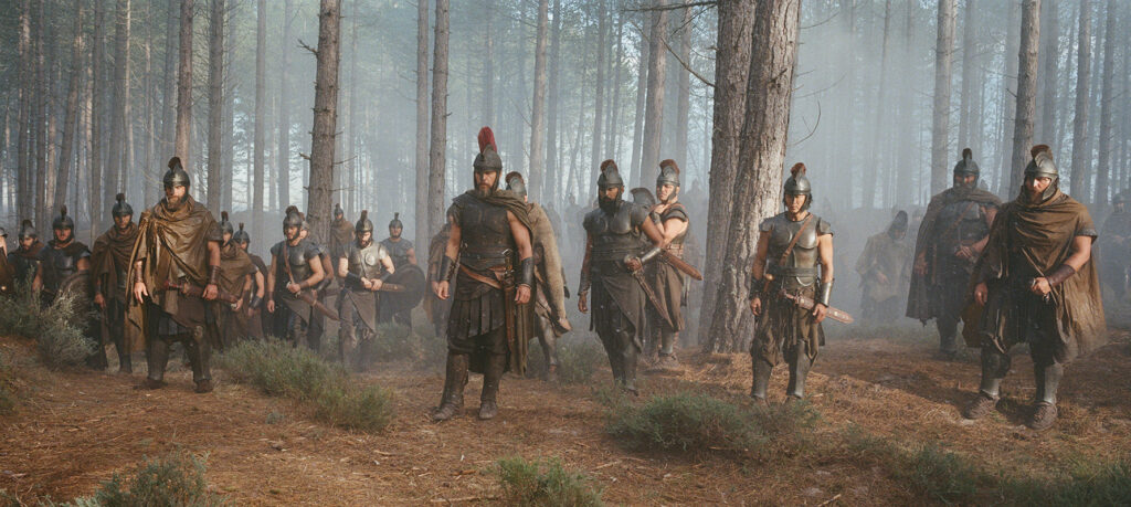Let me say the quiet part loudly: Christopher Nolan did not make a swords-and-sandals adventure. He made a war film wearing a myth as a mask, and it may be the most punishing, beautiful thing he has ever put on a screen. The Odyssey is his thirteenth feature, the first narrative film in history shot entirely on IMAX film, and already the biggest global launch of his career — an instant awards frontrunner that had the industry roaring from its first CinemaCon footage onward, in a year that suddenly has very little competition. Coming off Oppenheimer, Nolan has essentially made a companion piece in bronze: another story about a brilliant man whose single clever idea unleashes a horror the world cannot put back in the box. If Oppenheimer gave us the father of the atomic bomb, The Odyssey gives us his Bronze Age ancestor.
